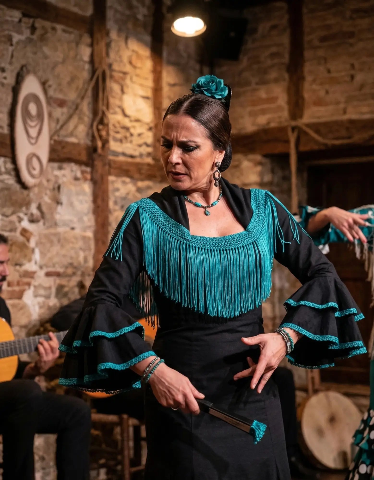 Mulher com vestido flamenco preto com franjas e renda em teal e acessório floral combinando destaca passamanarias na moda 2026