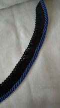 Cordão de algodão preto com vivo azul, em detalhe sobre tecido claro.