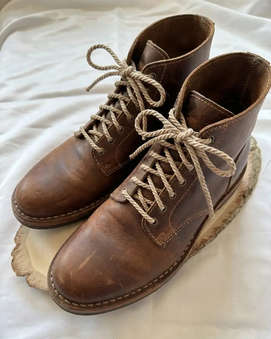 Pair of handcrafted brown leather boots with beige laces on white background