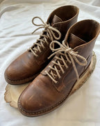 Pair of handcrafted brown leather boots with beige laces on white background
