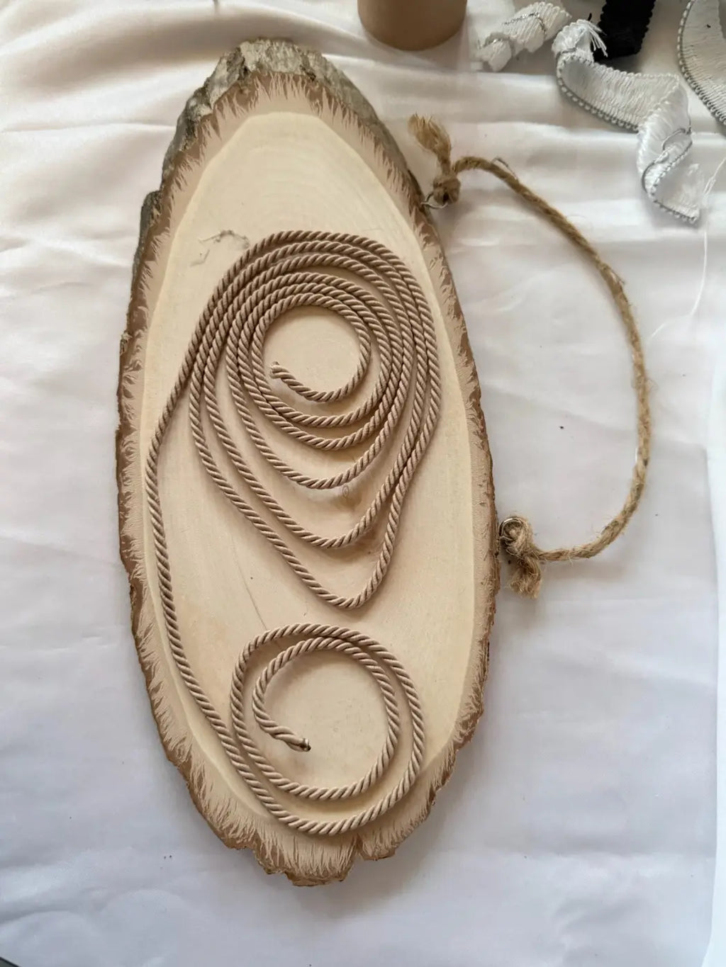 Beige twisted rope accessory coiled on rustic wood slice, luxury display product for storefront by L&L Concept Retail.