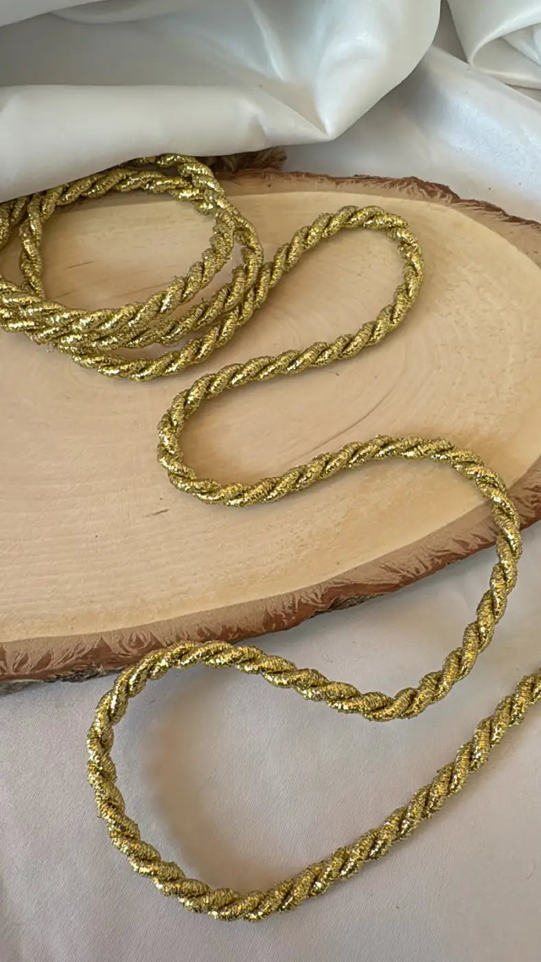 Cordão versalhes lurex premium dourado 5mm com brilho dourado encordoado repousando sobre fatia de madeira