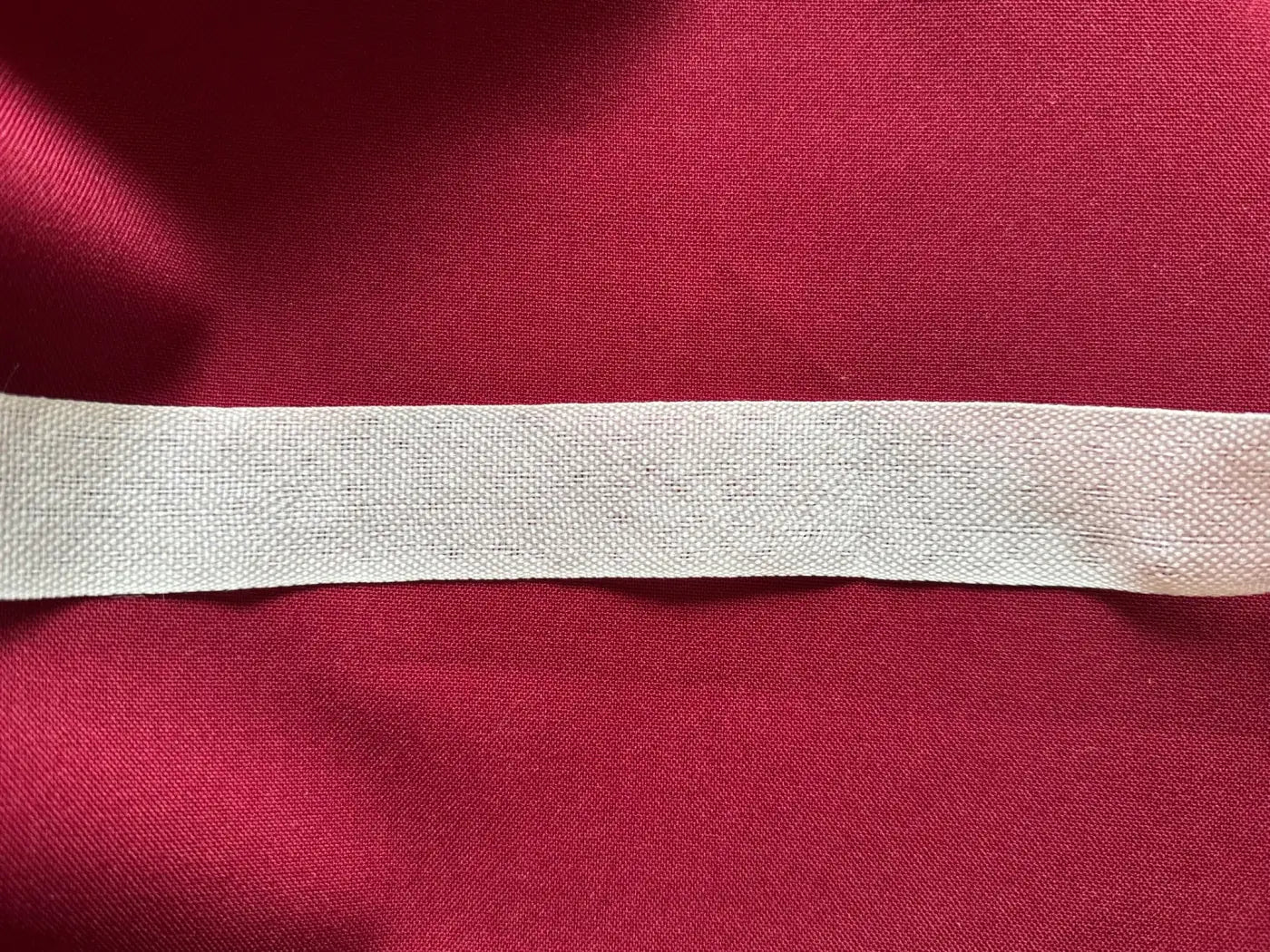 Fita nastro gorgorão poliéster 55mm branco com textura canelada e toque natural sobre tecido vermelho