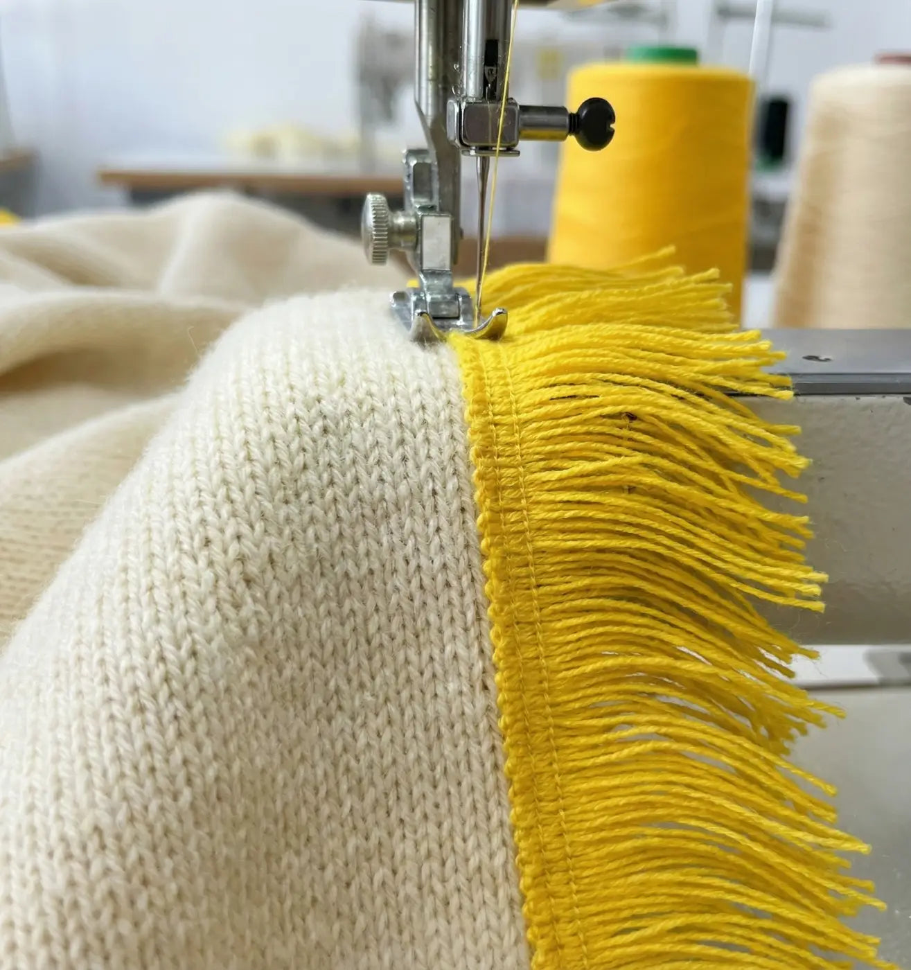 Franja héritage acrílico 100% 50mm amarela vibrante sendo costurada em tecido de malha creme com máquina de costura