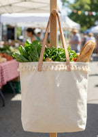 Cream-colored canvas tote bag with tan leather straps and white fringe trim from linha pura algodão 100% natural l&l